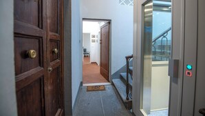 A hallway with a wooden door, a glass elevator door, and a tiled floor. - Mamo Florence - Macci Apartment (Florence)