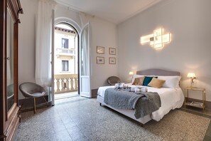 Quarto de hotel com uma cama, uma cadeira, uma mesinha de cabeceira e vista para a varanda externa.