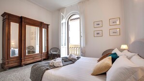 Een hotelkamer met een groot bed, een houten garderobe, een balkon met een balustrade en ingelijste foto’s aan de muur.