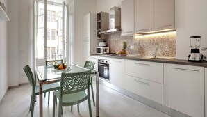Een moderne keuken met witte kastjes, een glazen eettafel en uitzicht naar buiten.