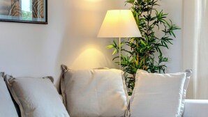 Ein modernes Wohnzimmer mit einer Couch, zwei Kissen, einer Lampe und einer Topfpflanze.