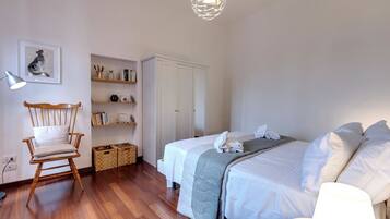 A bedroom with a bed, a chair, a desk, a lamp, and a shelf with books and decorative items.