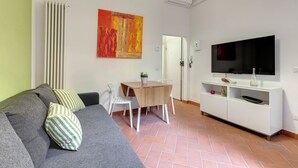 A living room with a grey sofa, a wooden dining table, and a TV on a white cabinet. - Mamo Florence - Maruffi Apartment (Florence)
