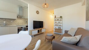 Un salon moderne comprenant un canapé, un téléviseur, une table à manger et un coin cuisine avec un évier et une cuisinière.
