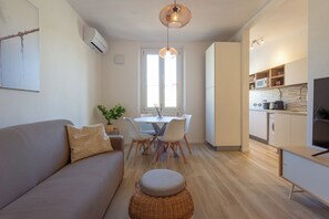 A modern kitchen with white cabinets, a microwave, and a sink. There is a dining area with a table and chairs, and a living room with a sofa and a TV. - Mamo Florence - Mosse Leopolda Apartment (Florence)
