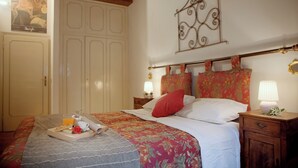A bedroom with a bed, a nightstand, a wooden headboard, a wardrobe, and a decorative wall piece. - Mamo Florence - Palazzo Spinelli Apartment (Florence)