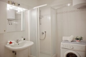 A bathroom with a white sink, mirror, shower, and washing machine.