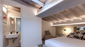 A bedroom with a wooden ceiling, a bed with white bedding, a bedside table with a lamp, and a small potted plant. - Mamo Florence - Parione Apartment (Florence)