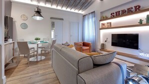 A modern living room with a sofa, a dining table with chairs, a television, and a 'SUPER' sign on the wall. - Mamo Florence - Parione Apartment (Florence)