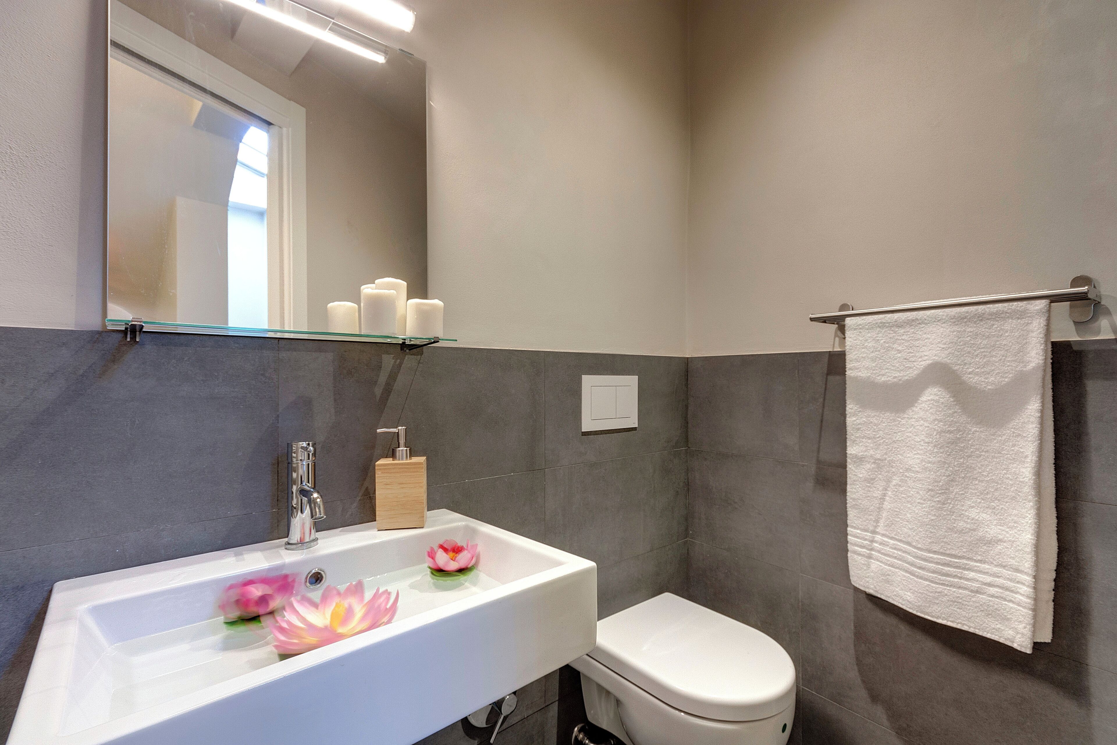 A bathroom with a white sink, a toilet, a glass shelf above the sink, and a towel hanging on a rack.