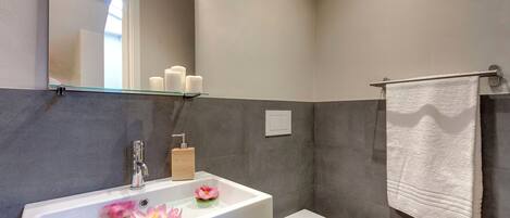 A bathroom with a white sink, a toilet, a glass shelf above the sink, and a towel hanging on a rack.
