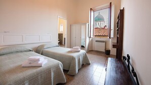 Een hotelkamer met twee bedden, een houten bankje, een radiator en een lijst met een afbeelding van een gebouw.
