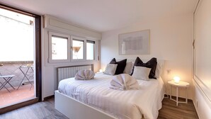 Ein Schlafzimmer mit Bett, Kissen, Nachttisch, Fenster und einer Tür zu einem Außenbereich.