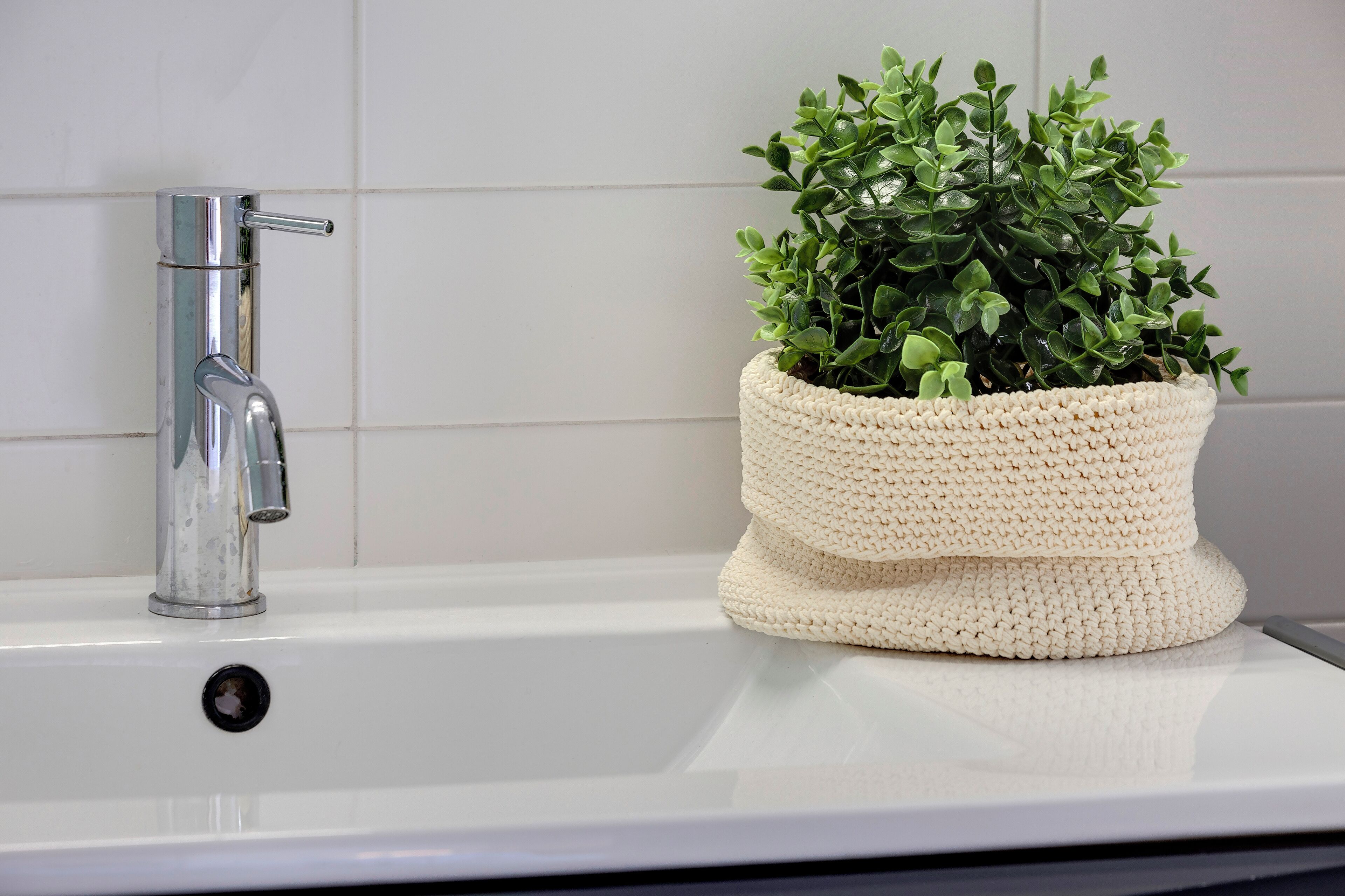 Un évier blanc avec un robinet chromé et une plante en pot, le pot étant blanc et texturé.