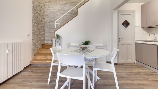 Eine moderne Küche mit weißen Schränken, einer Holztreppe und einem Essbereich mit weißen Stühlen und einem runden Tisch.