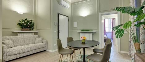 Une pièce comprenant un canapé, une table à manger avec des chaises, une plante en pot et un radiateur.