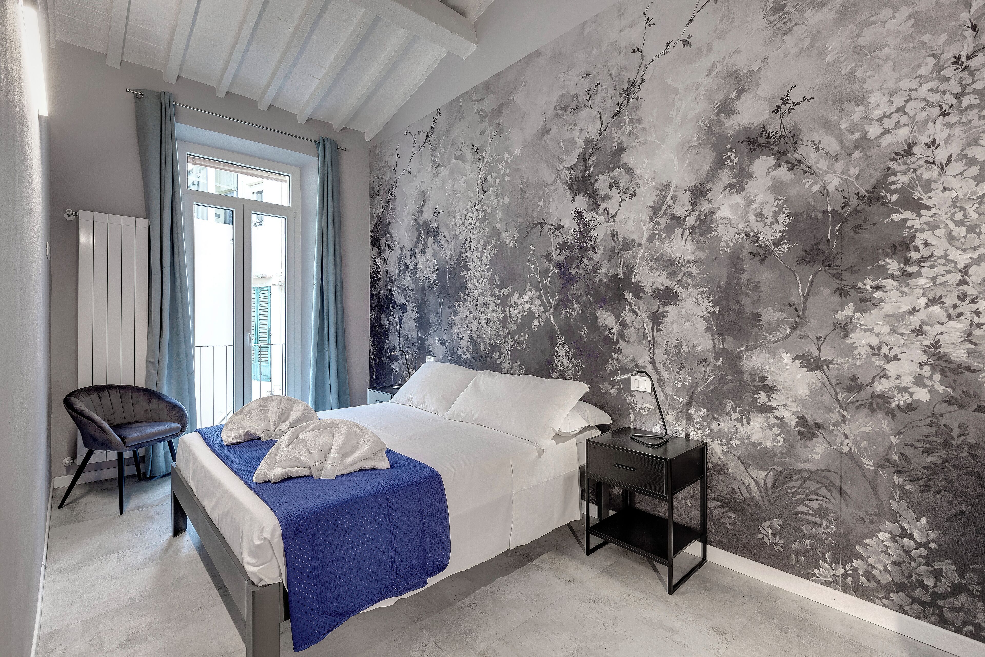 A bedroom with a bed, a chair, a nightstand, and a window with curtains.