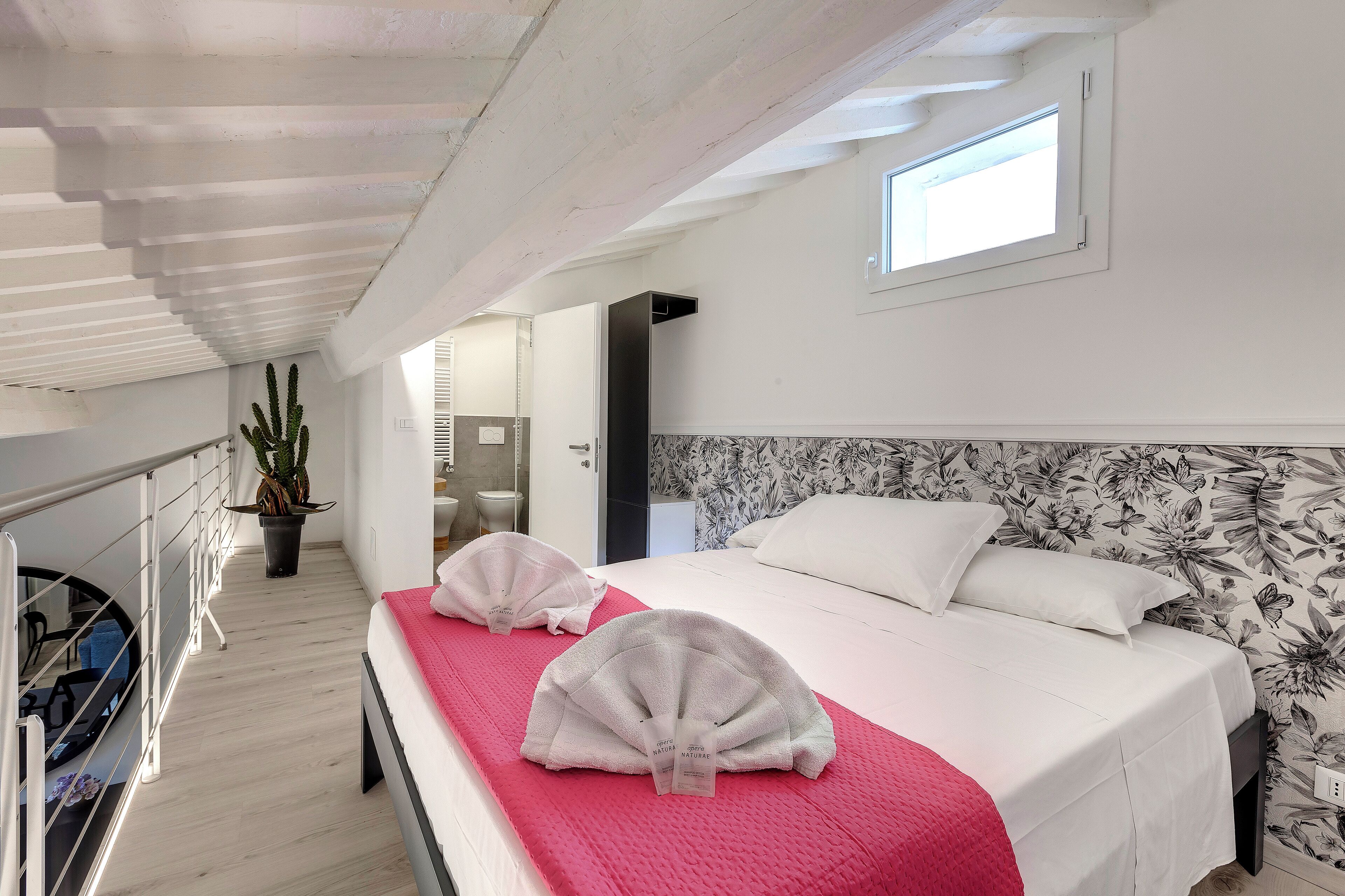 A hotel room with a large bed, a red blanket, and a potted plant.