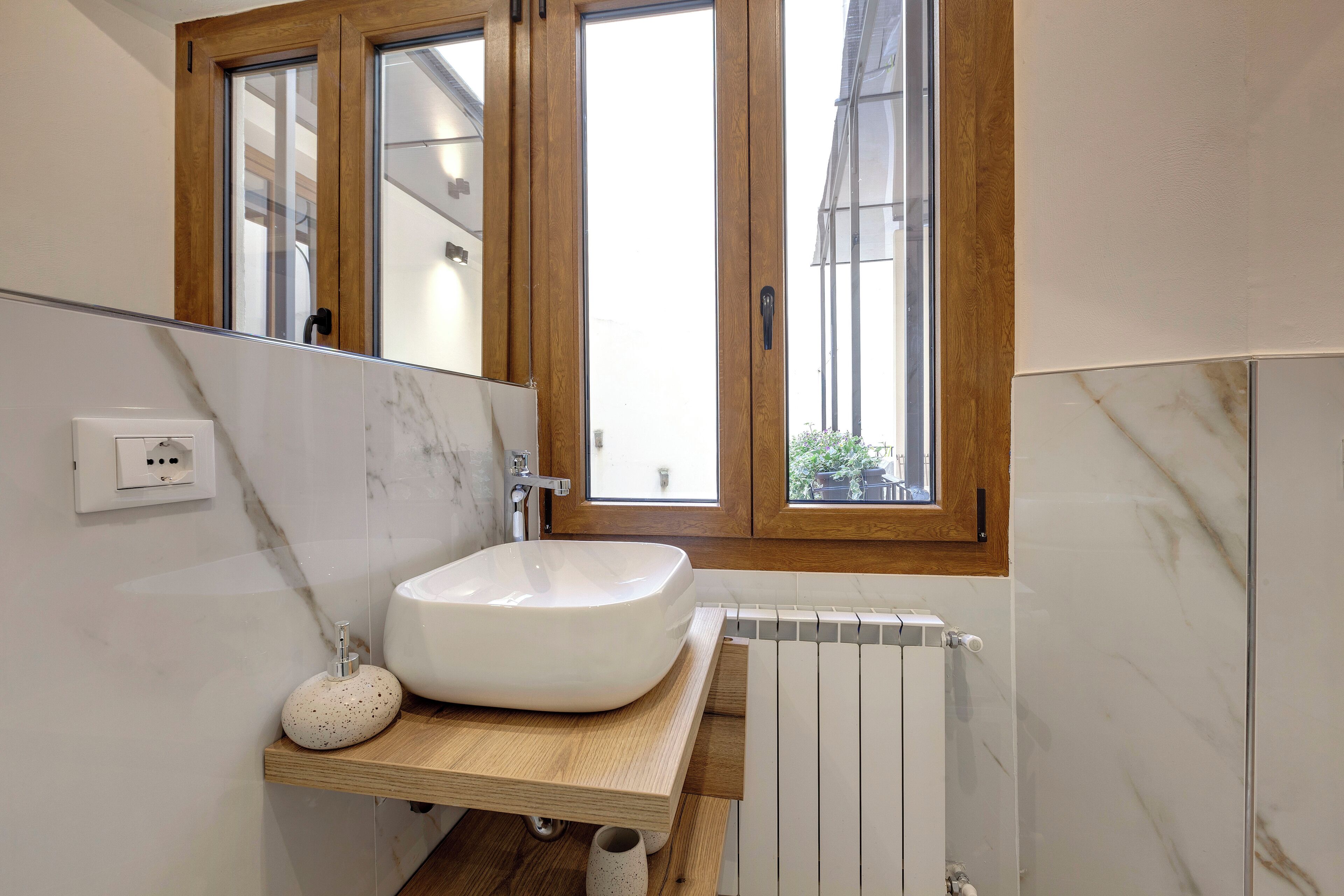 A modern bathroom with a large white sink, wooden countertop, and a window with a view of buildings outside.