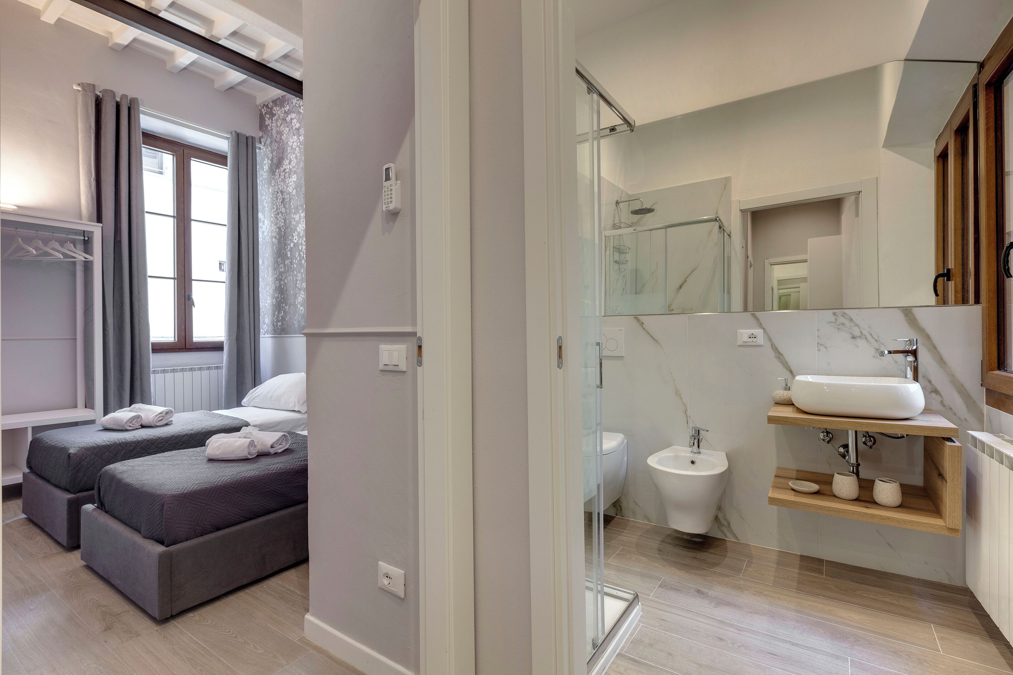A modern hotel room with two beds, a bathroom with a glass shower, and a marble-tiled vanity.