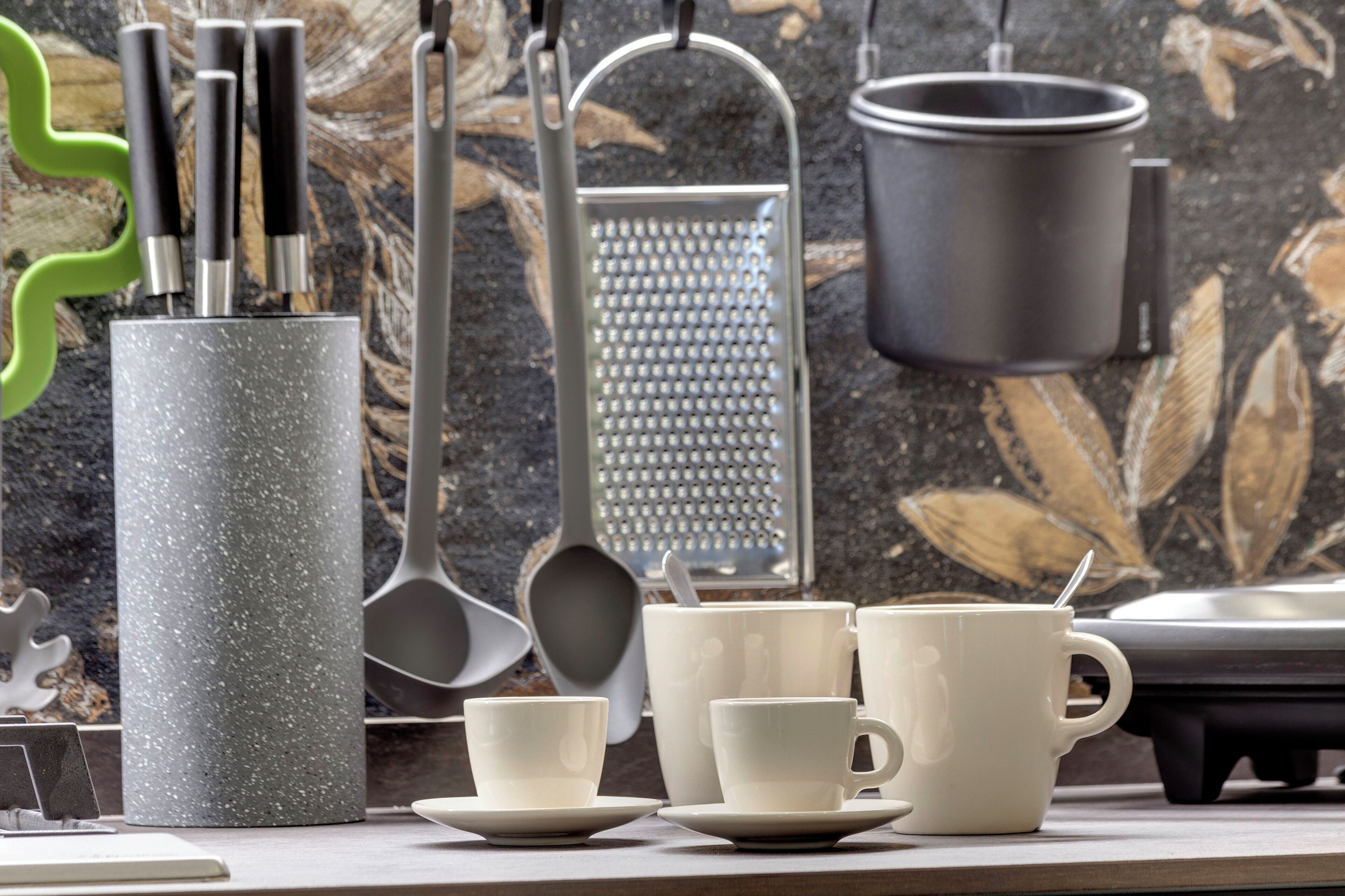 A kitchen counter with various utensils and cookware, including a grater, a pot, and several cups and plates.