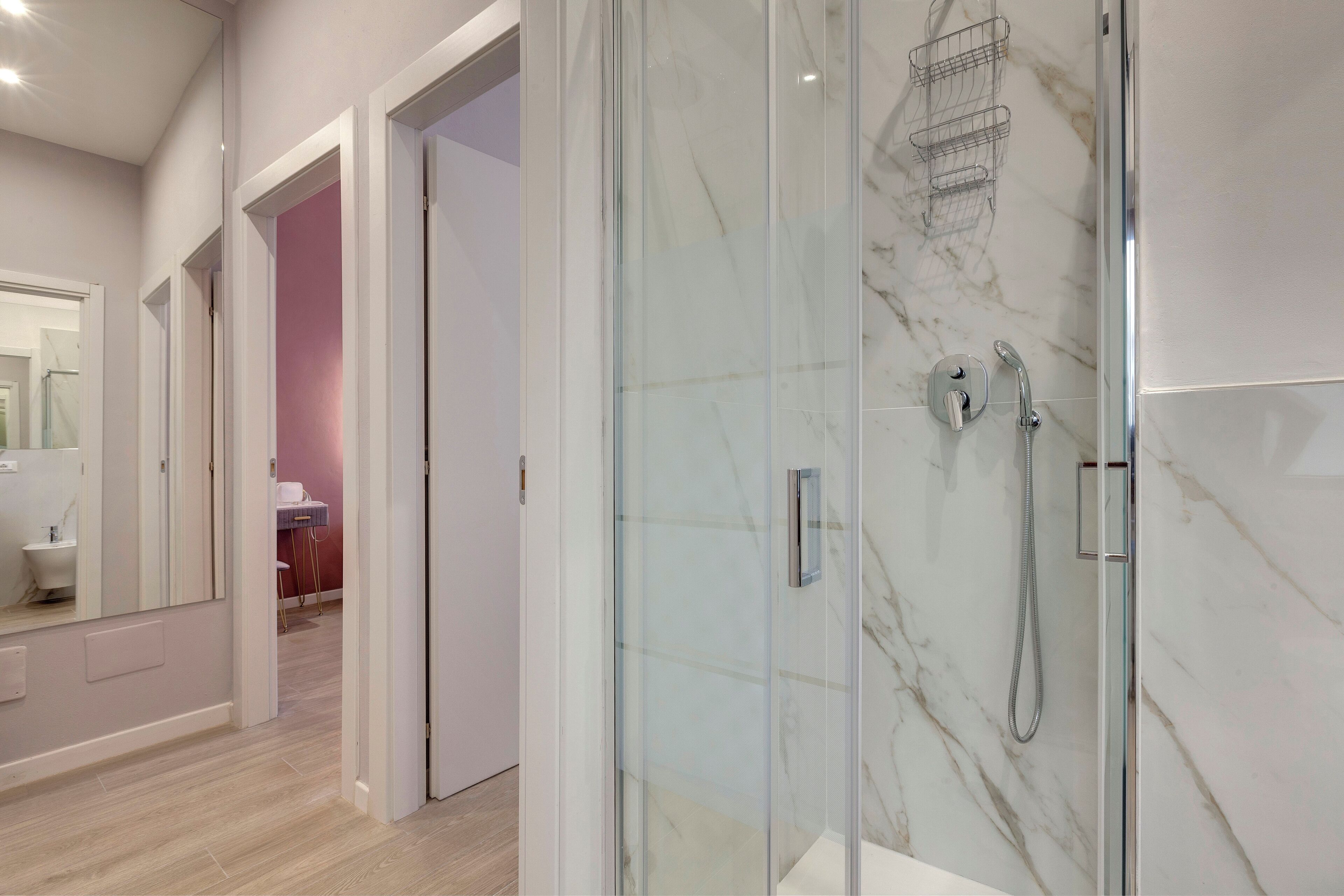 A modern bathroom with a glass-enclosed shower, marble tiles, and a visible toilet in the background.