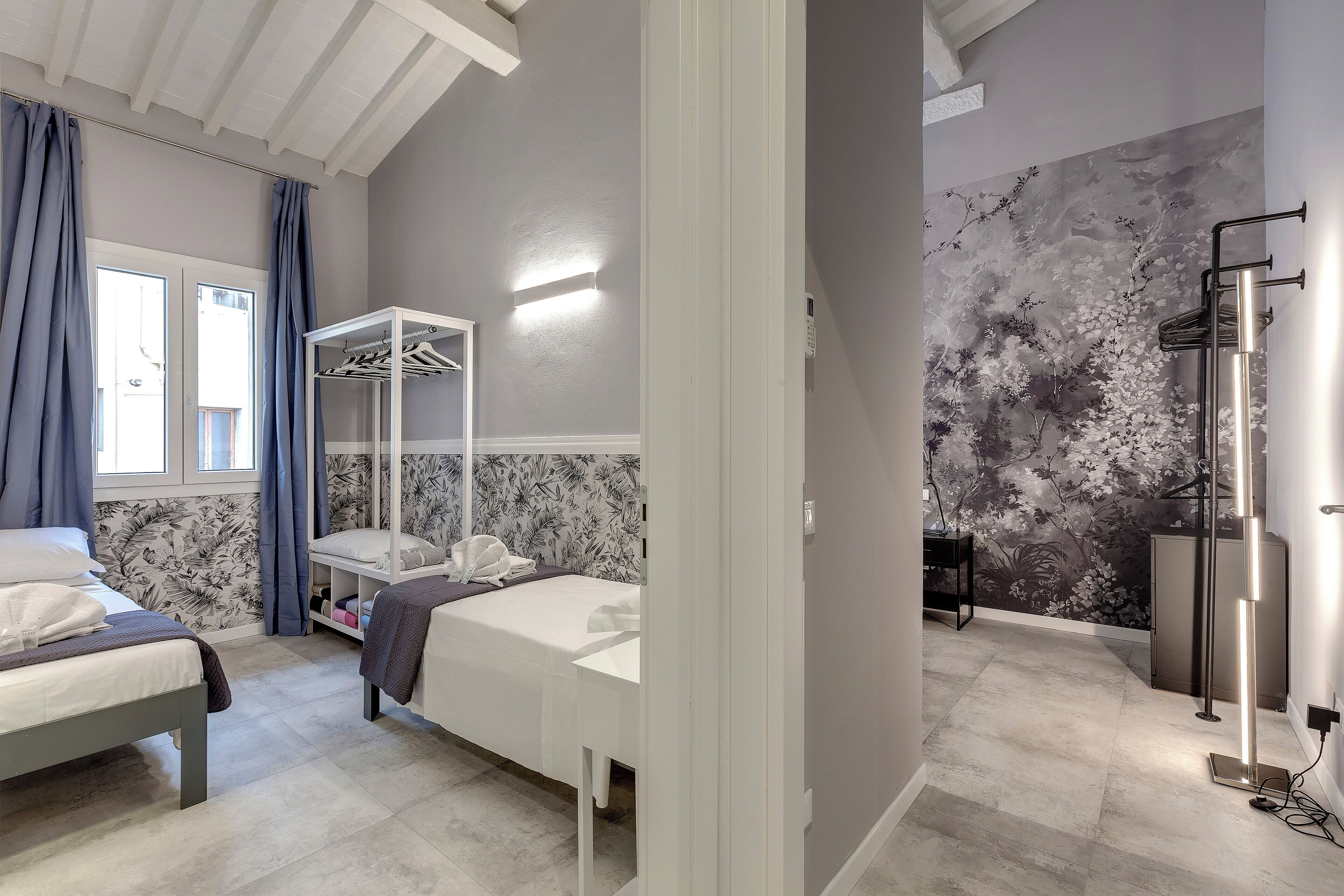 Ein Hotelzimmer mit zwei Betten, einem Kleiderschrank, einer Duschkabine und einer Wand mit floralem Wandbild.