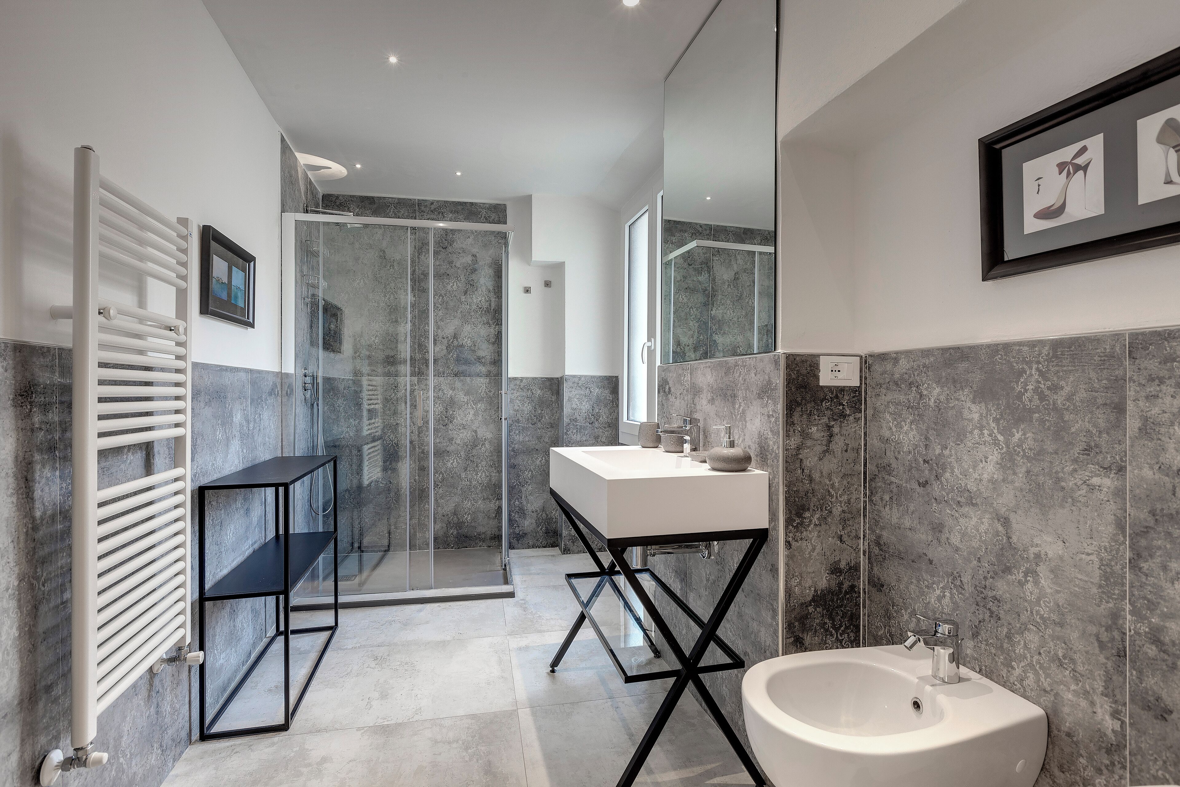 Une salle de bain moderne avec une douche à l’italienne en verre, un lavabo blanc et une étagère en métal noir.