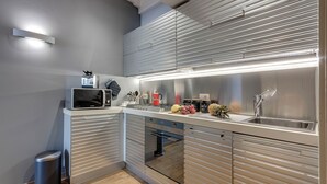 Una cucina moderna con elettrodomestici in acciaio inossidabile, un forno a microonde, un lavandino e un piano di lavoro con frutta e un bollitore.