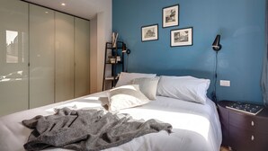 Una camera da letto con un letto, un comodino, una lampada a parete e quadri appesi al muro.