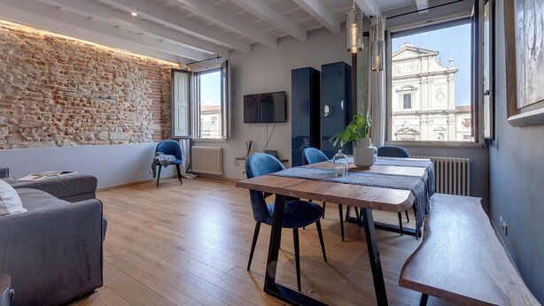 Un soggiorno moderno con parete in pietra, pavimento in legno e zona pranzo con sedie blu e tavolo in legno.