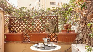 Une petite terrasse extérieure avec une table dressée pour deux personnes, une cafetière, des tasses et un livre.
