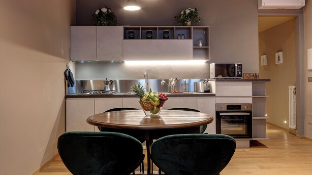 Une cuisine moderne avec un coin repas, comprenant une table ronde en bois, deux chaises vertes et un saladier à fruits.