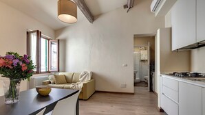 A modern kitchen with white cabinets, a dining area with a table and chairs, and a living area with a sofa. - Mamo Florence - Santa Reparata Apartment (Florence)