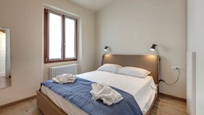 A bedroom with a bed, a window, a radiator, and a wall-mounted lamp. - Mamo Florence - Santa Reparata Apartment (Florence)
