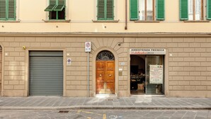 A building with a closed shutter door, a wooden double door entrance, and a sign for "ASSISTENZA TECNICA DB elettronica COMPUTER". - Mamo Florence - Santa Reparata Apartment (Florence)