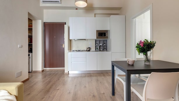 A modern kitchen with white cabinets, a microwave, and a dining area with a table and chairs. - Mamo Florence - Santa Reparata Apartment (Florence)