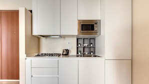 A compact kitchen with white cabinets, a microwave, a kettle, and a small shelf with plants. - Mamo Florence - Santa Reparata Apartment (Florence)