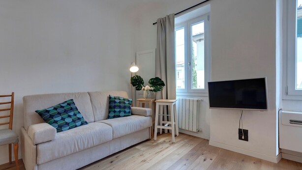 En stue med sofa, fjernsyn, et lille bord og et vindue med gardiner.