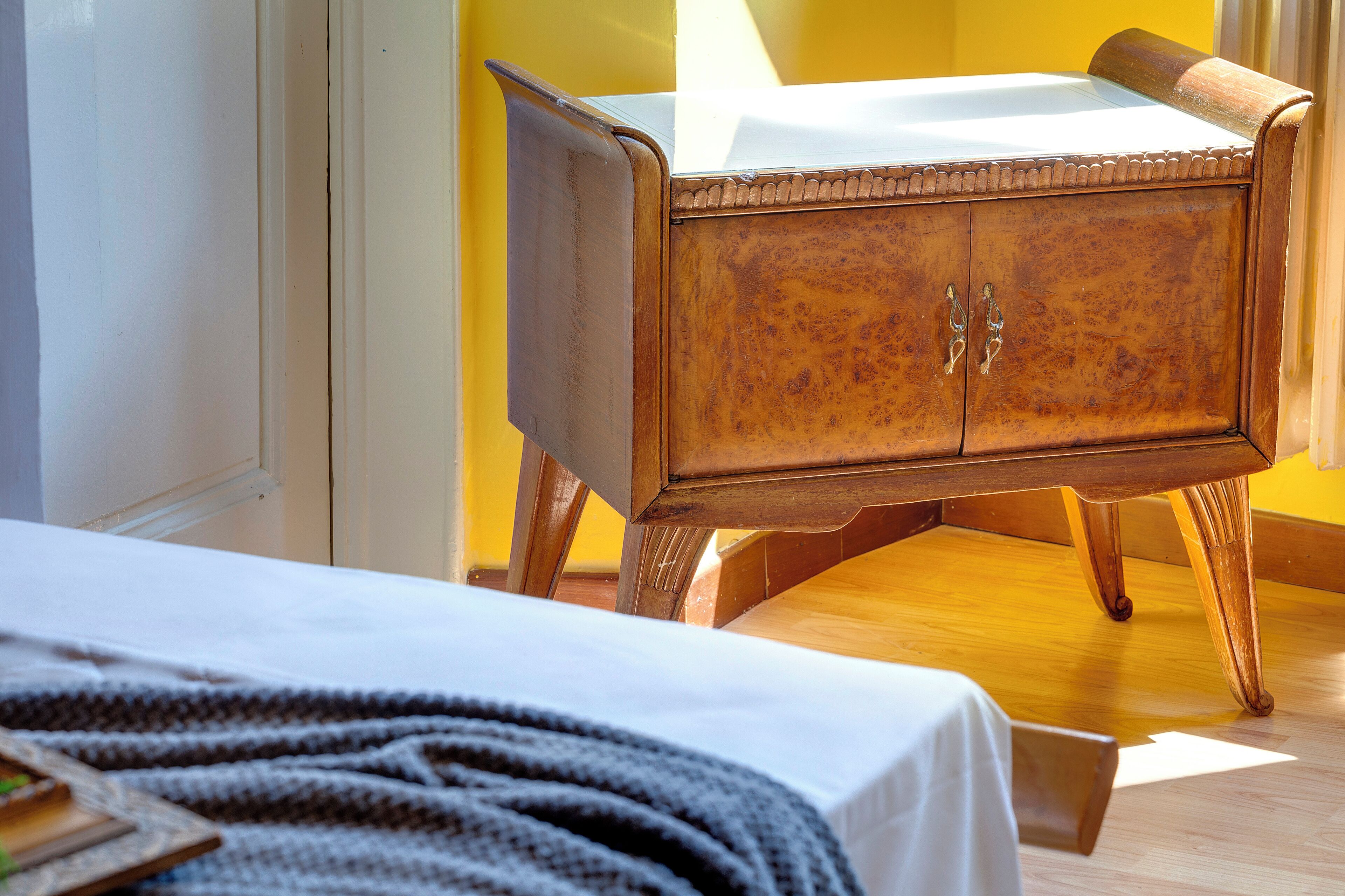 A wooden cabinet with a white cloth on top, positioned against a yellow wall.
