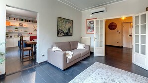 Una sala de estar con un sofá, una mesa de centro y una estantería. Hay un cuadro en la pared y una puerta que da a otra habitación.