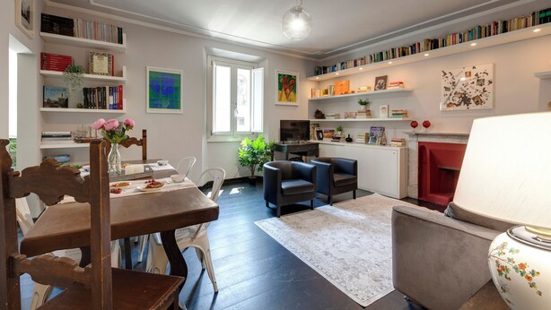 Una habitación bien iluminada con una mesa de comedor, sillas, un sofá y una estantería llena de libros.