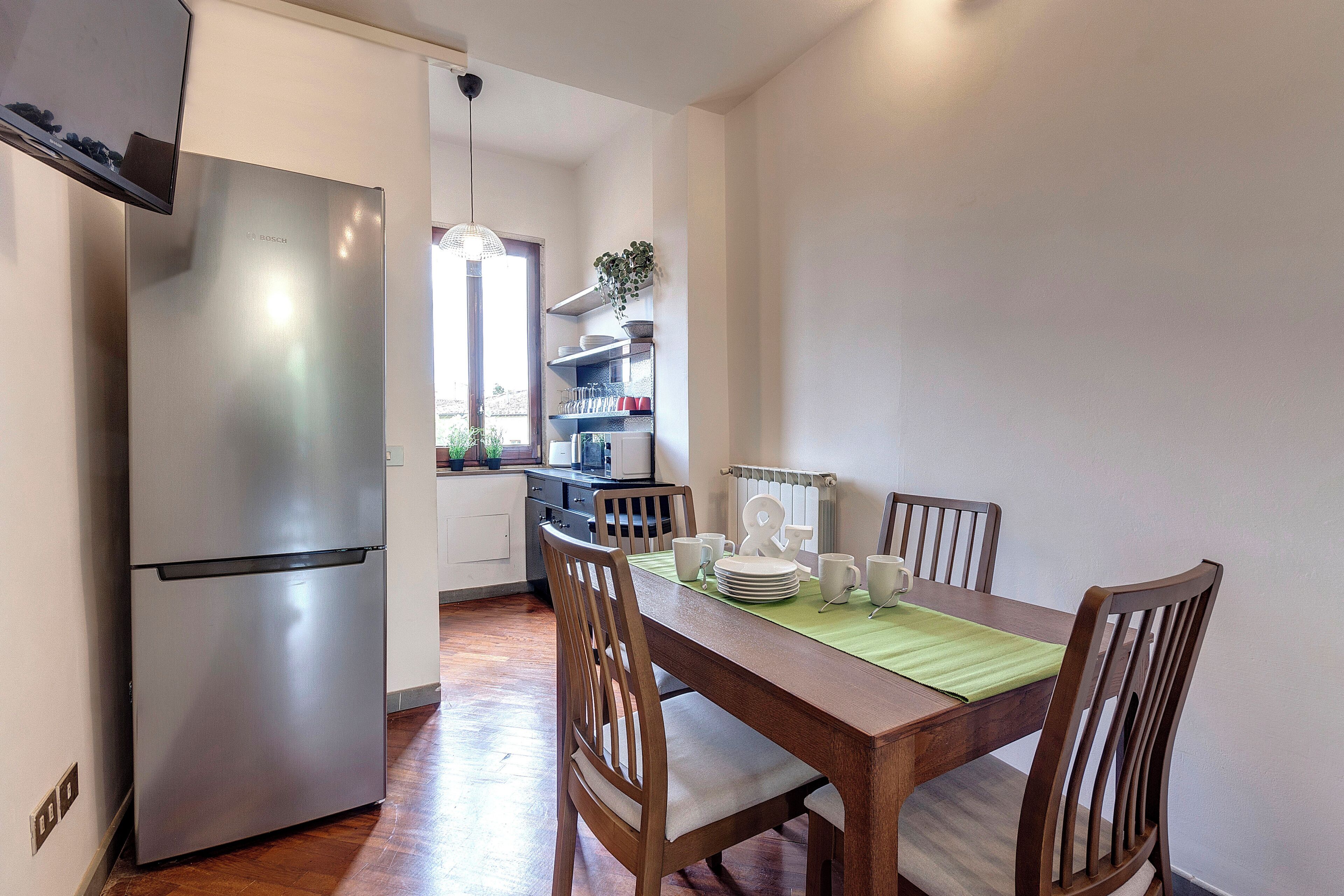 A modern kitchen with a stainless steel refrigerator, wooden dining table, and chairs.