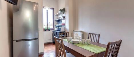 A modern kitchen with a stainless steel refrigerator, wooden dining table, and chairs.