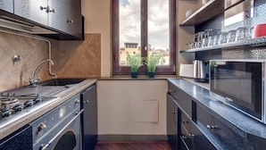 A compact kitchen with a stove, sink, and microwave. There is a window with a view of buildings and plants outside. - Mamo Florence - Spirito19 Apartment (Florence)