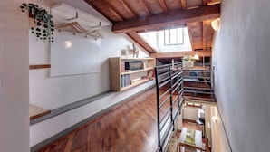 A spacious loft with wooden floors, a mezzanine level, and a view of the kitchen below. - Mamo Florence - Spirito19 Apartment (Florence)