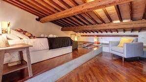 A spacious loft bedroom with a high ceiling, wooden beams, a large bed, a sofa, and a small table. - Mamo Florence - Spirito19 Apartment (Florence)