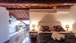 A bedroom with a wooden ceiling, a bed with a dark quilt, two bedside lamps, and a nightstand with a lamp. - Mamo Florence - Spirito19 Apartment (Florence)