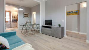 Uma sala de estar moderna com um sofá azul, uma mesa de jantar de vidro e um móvel de entretenimento cinzento.