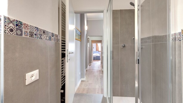 Um corredor com azulejos estampados, área de chuveiro e porta que dá para um quarto.